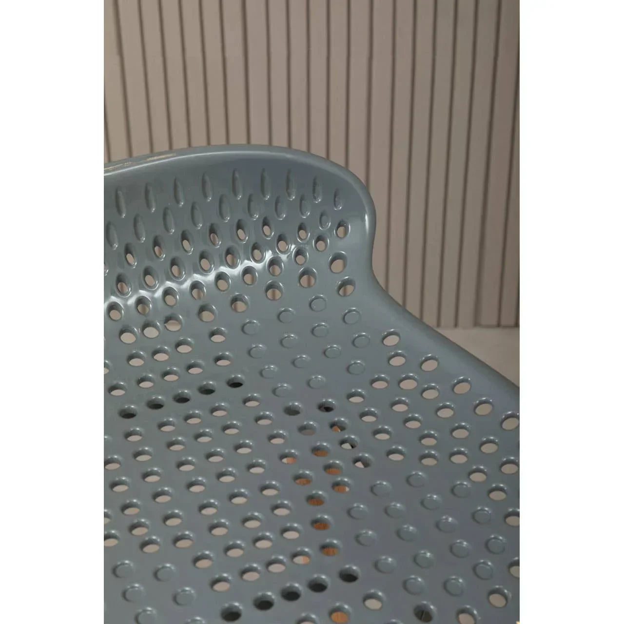 Closeup of grey perforated plastic chair with curved backrest against vertical slat wall