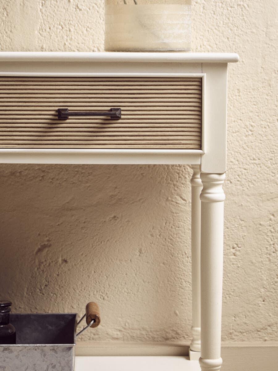 Cream console table with ribbed wood drawer and black metal handle against textured wall