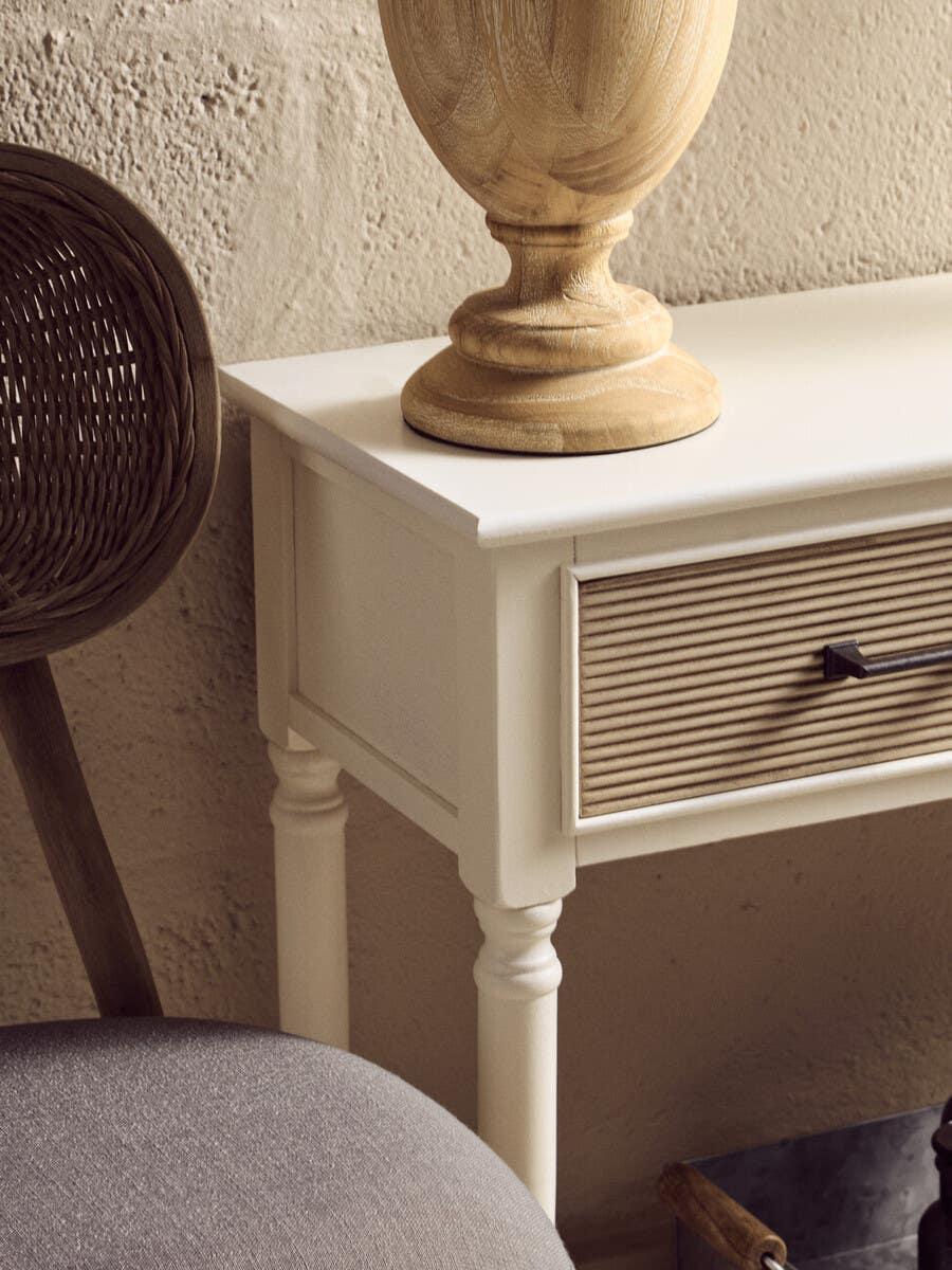 Cream console table with turned legs and ribbed drawer front beside rattan chair
