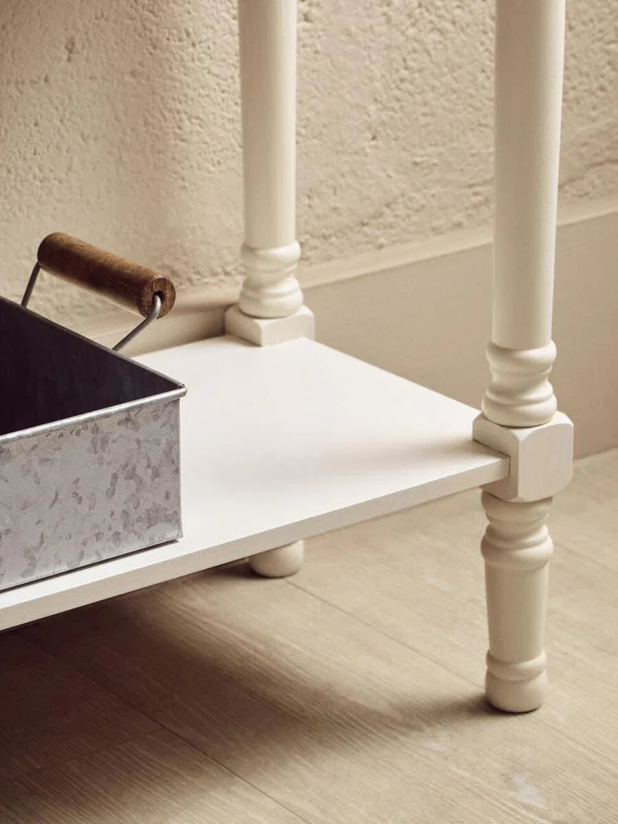 Close view of cream painted wooden furniture leg on light wood floor, storage shelf underneath