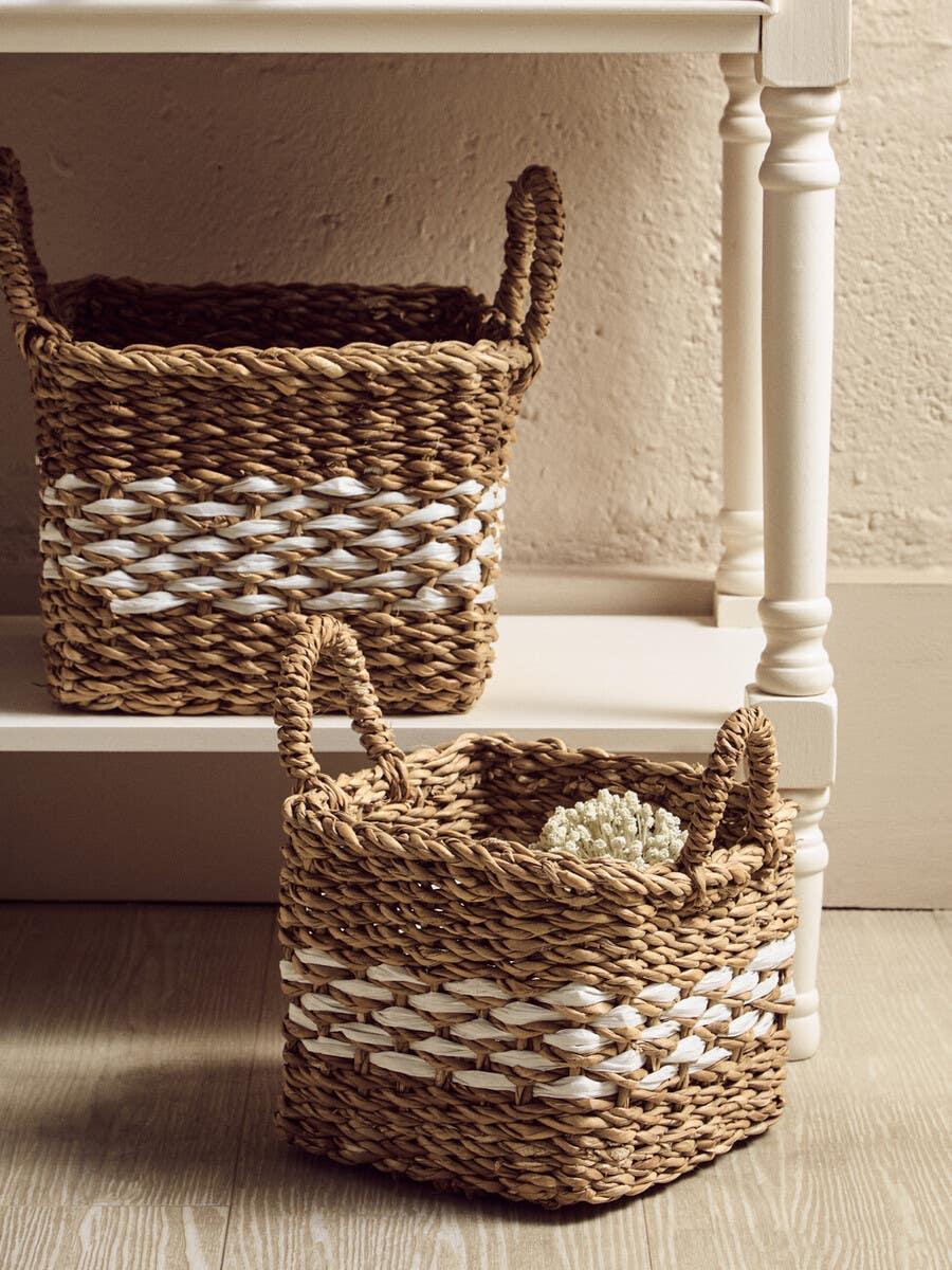 Square woven storage baskets with handles and white accent stripe on wooden floor