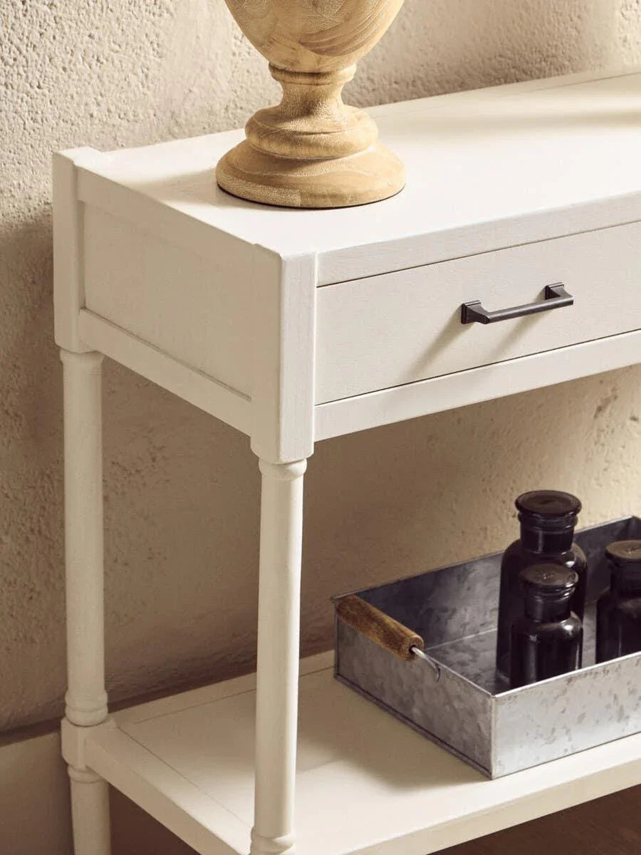 White console table with drawer, black handle, and lower shelf holding metal tray and bottles