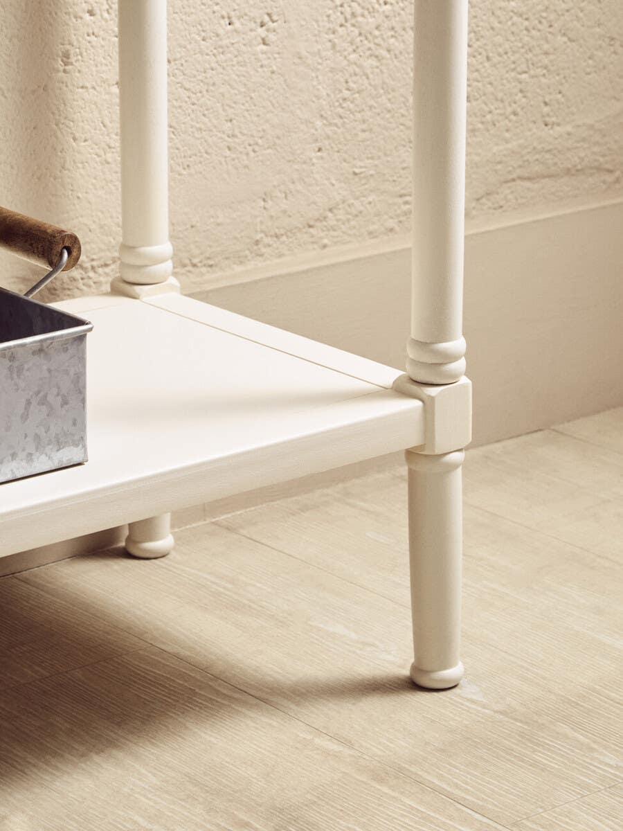 Close up of cream painted wooden table leg and lower shelf on light wood floor
