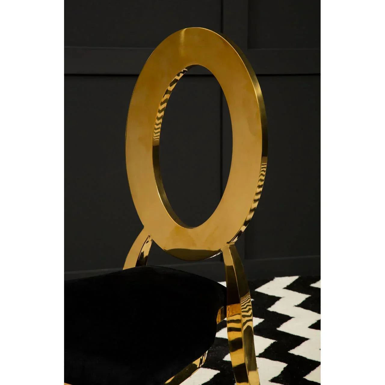 Gold metal dining chair with oval back and black velvet seat on chevron rug
