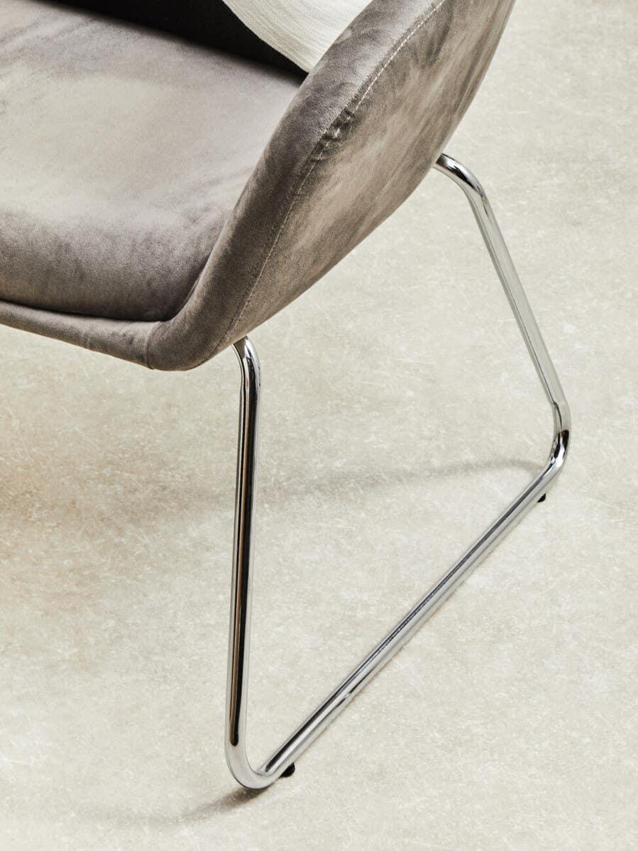 Grey velvet dining chair with chrome metal legs on light tiled floor