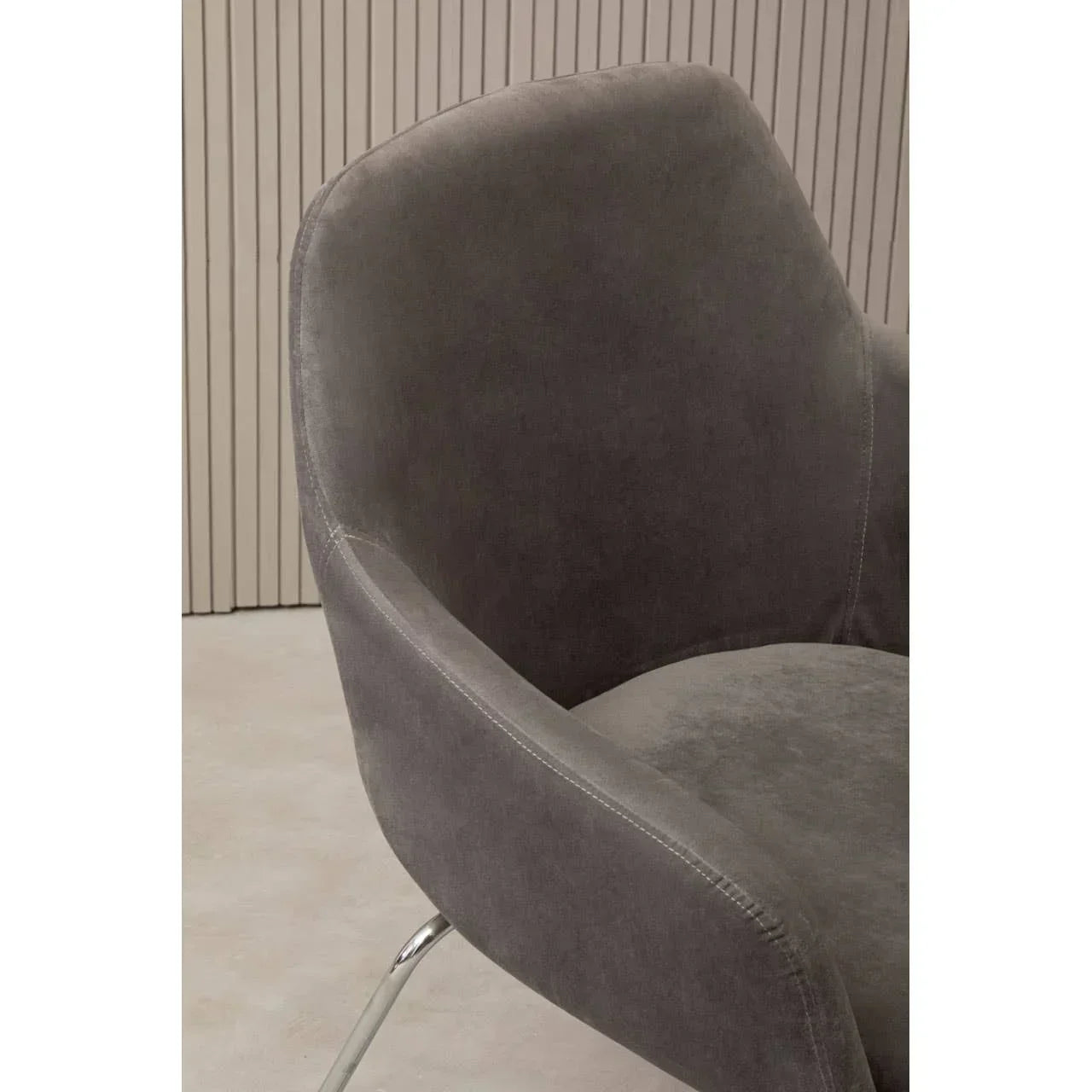 Grey velvet accent chair with curved backrest and chrome legs, close-up side view
