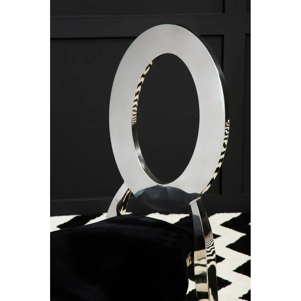 Modern dining chair with oval chrome backrest and black velvet seat on patterned rug