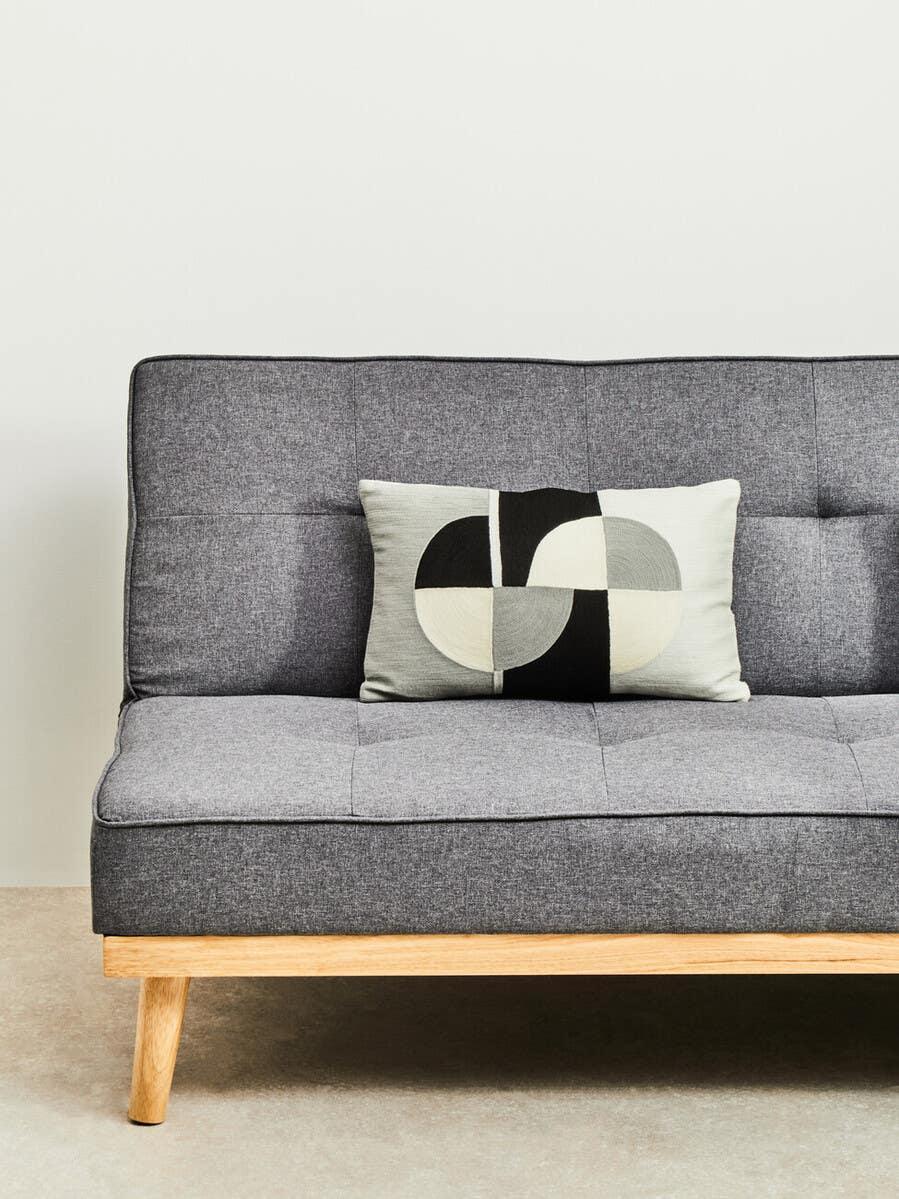 Grey fabric sofa with wooden legs and a geometric black and cream cushion on seat