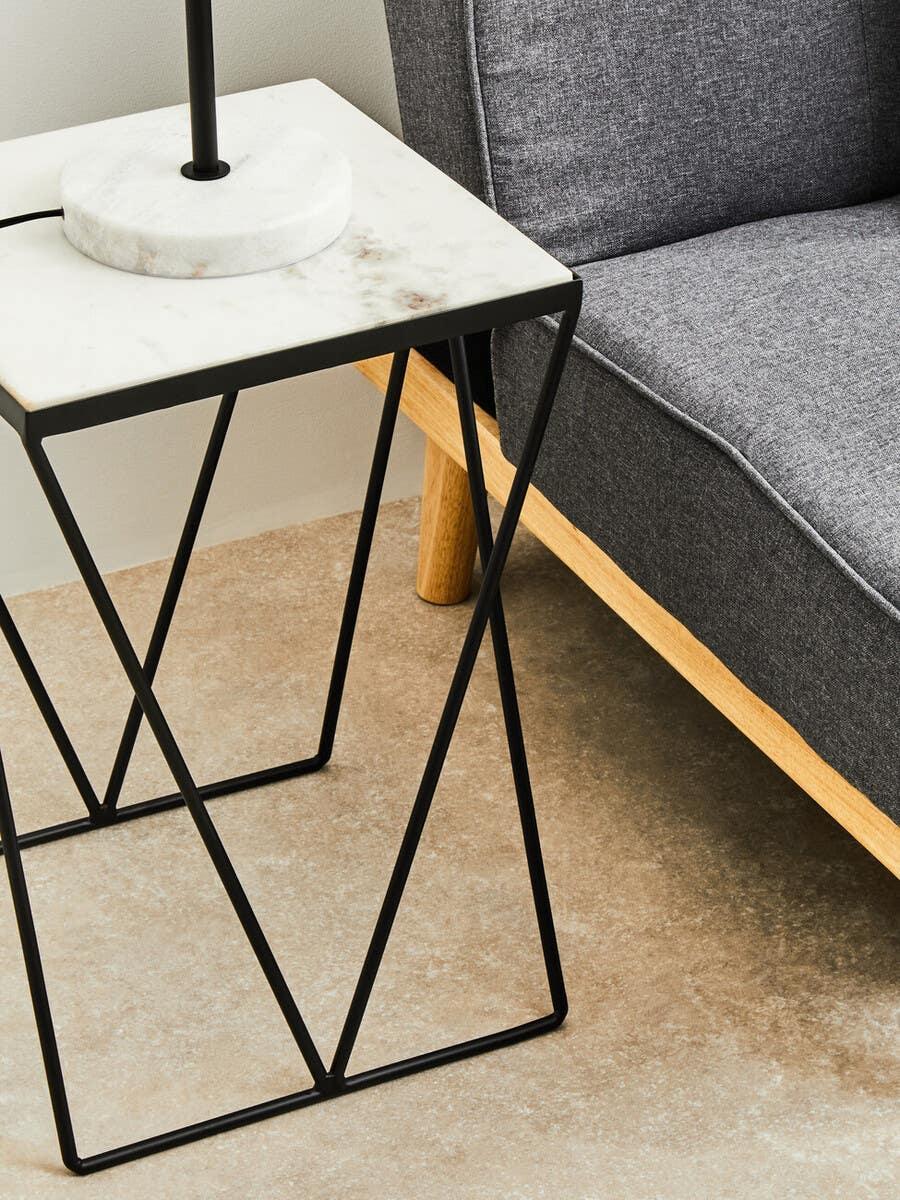 Marble top side table with black metal frame beside grey fabric sofa on wooden legs