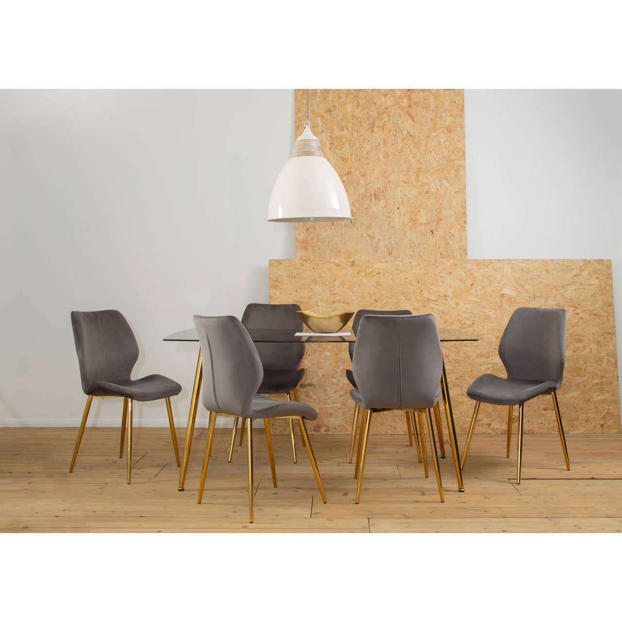 Smoked glass dining table surrounded by six upholstered chairs with wooden legs, set against a light-colored wall and a textured wooden backdrop. A pendant light hangs above the table, illuminating the scene. The floor is made of light wood planks