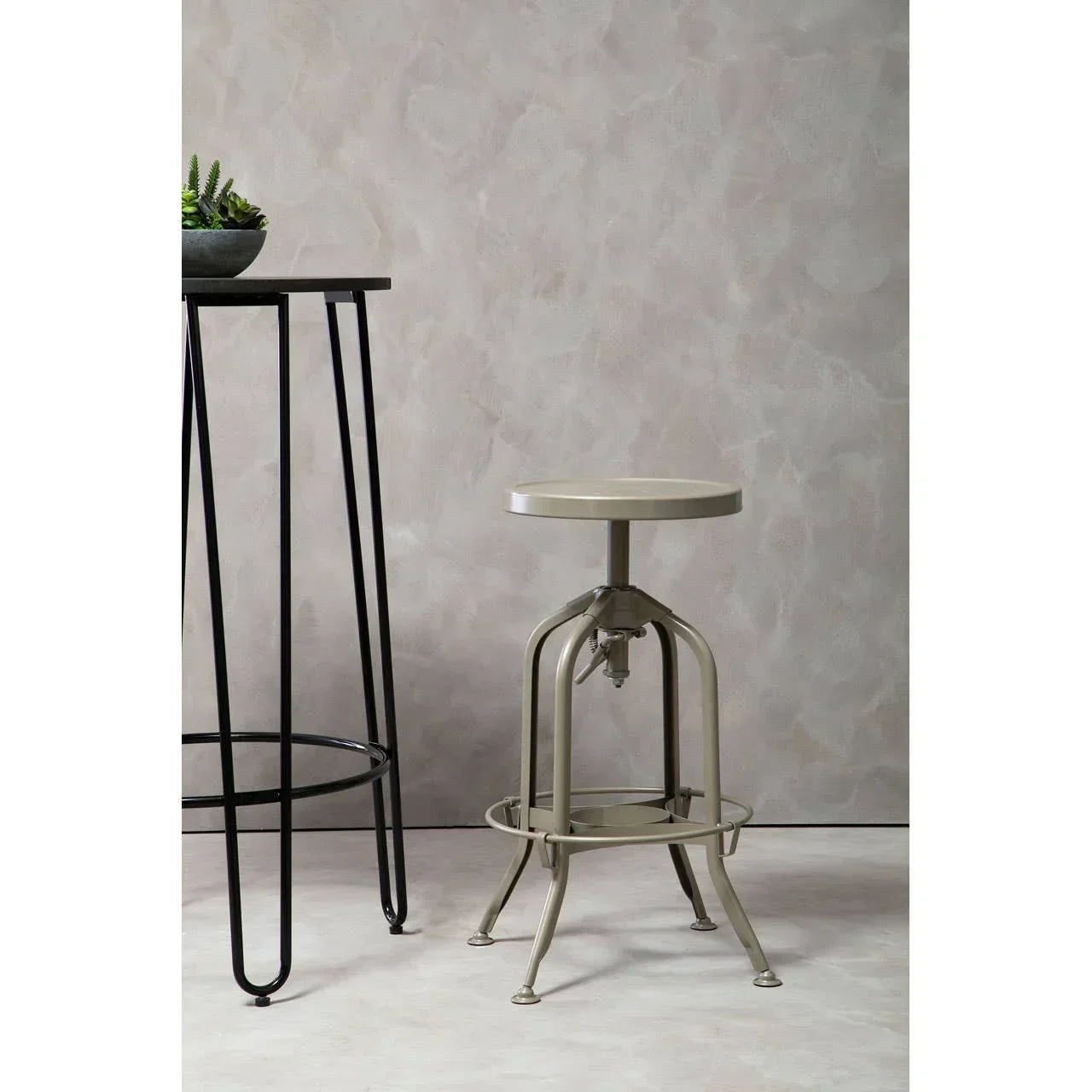 Industrial metal bar stool next to black metal plant stand against neutral wall