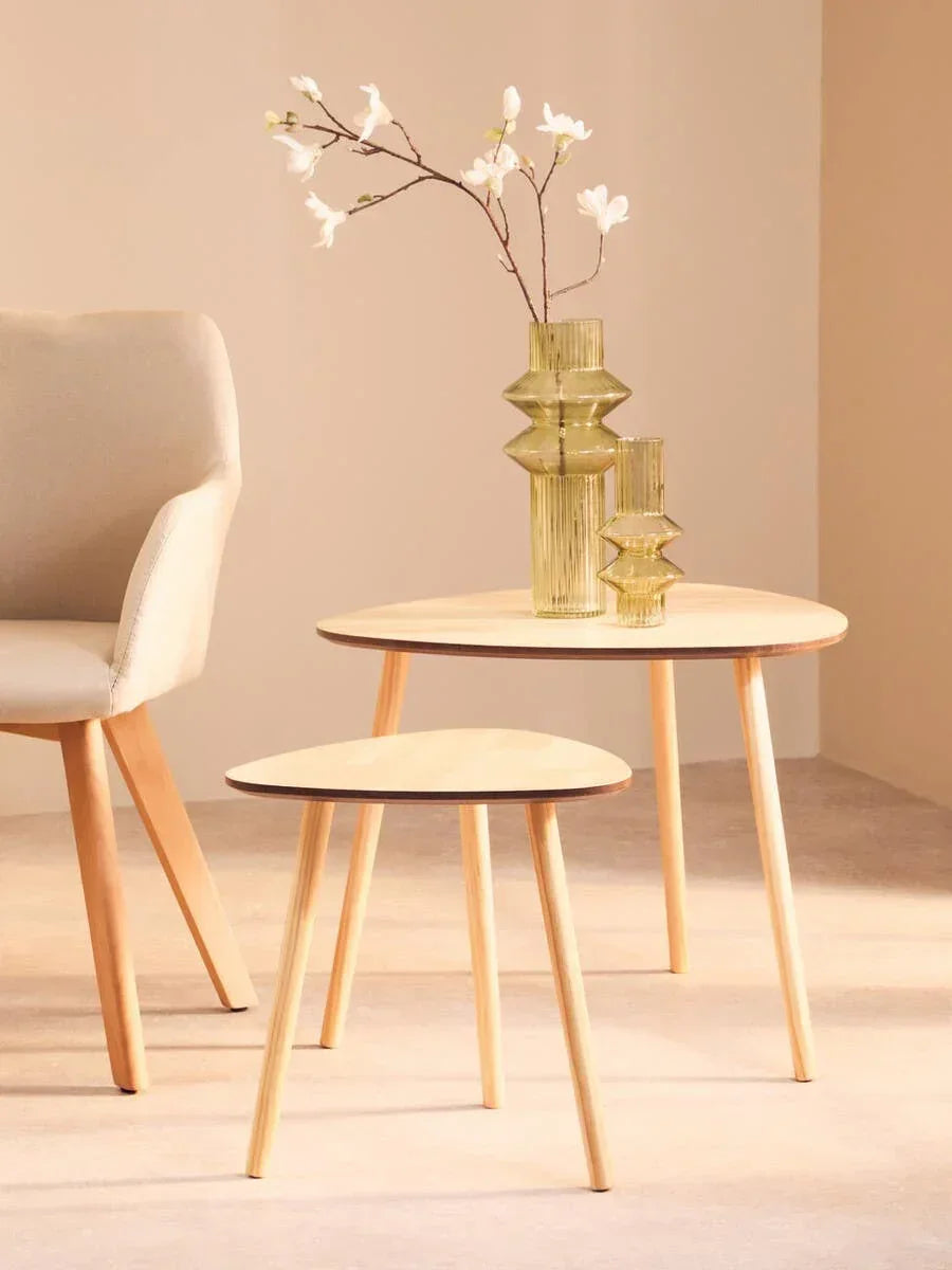 Set of two light wood side tables with glass vases beside beige upholstered chair