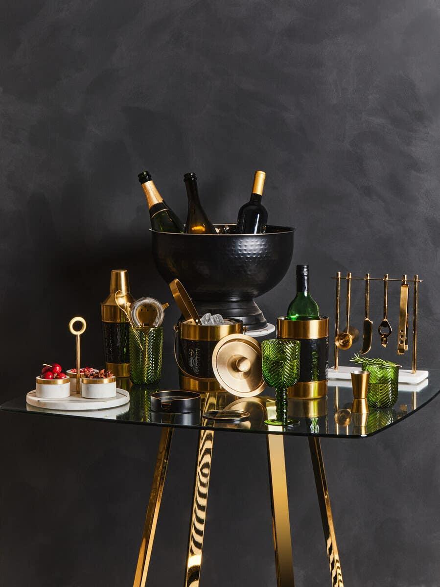 Glass bar table with gold legs, wine cooler, barware set, green glasses, and cocktail accessories