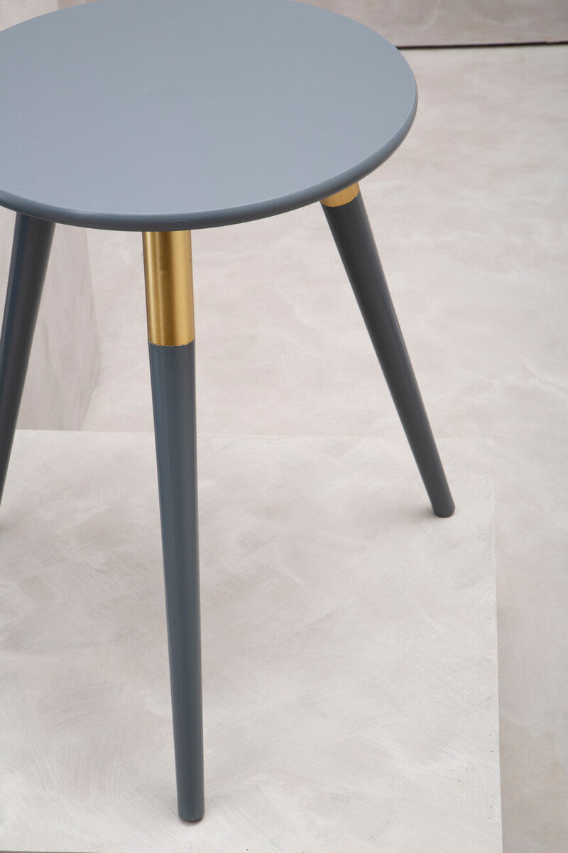 Round dark grey side table with three tapered legs, two of which have gold accents near the top. The table is placed on a light-colored floor, showcasing a minimalist design
