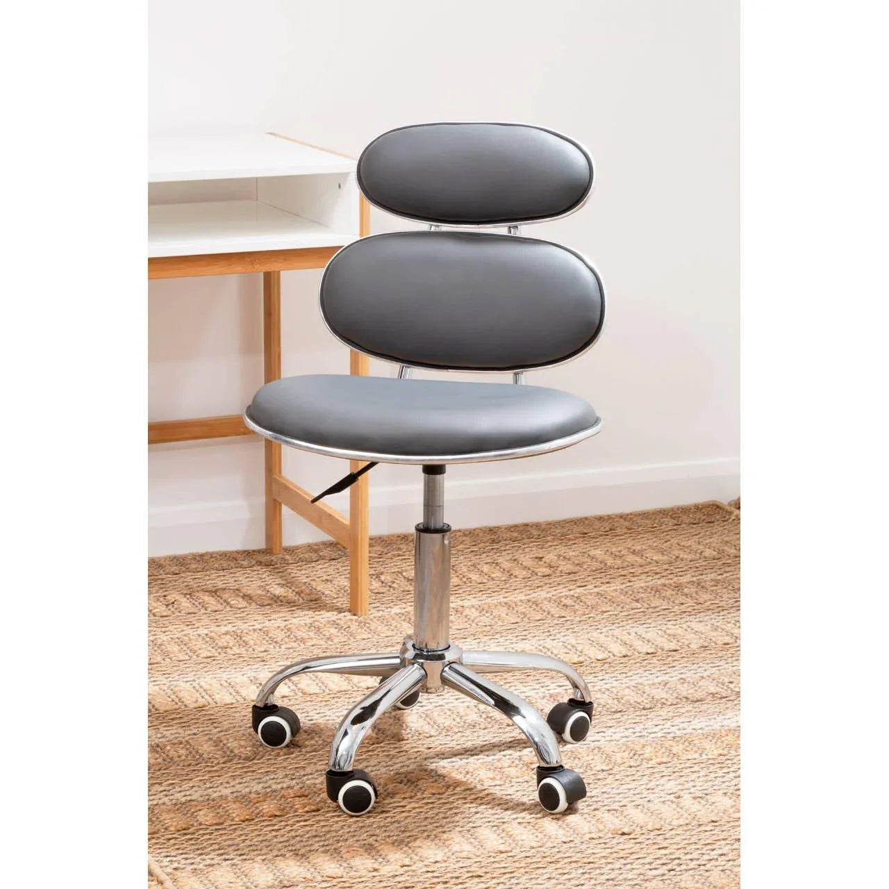 Grey office chair with chrome base and wheels on woven rug beside wooden desk