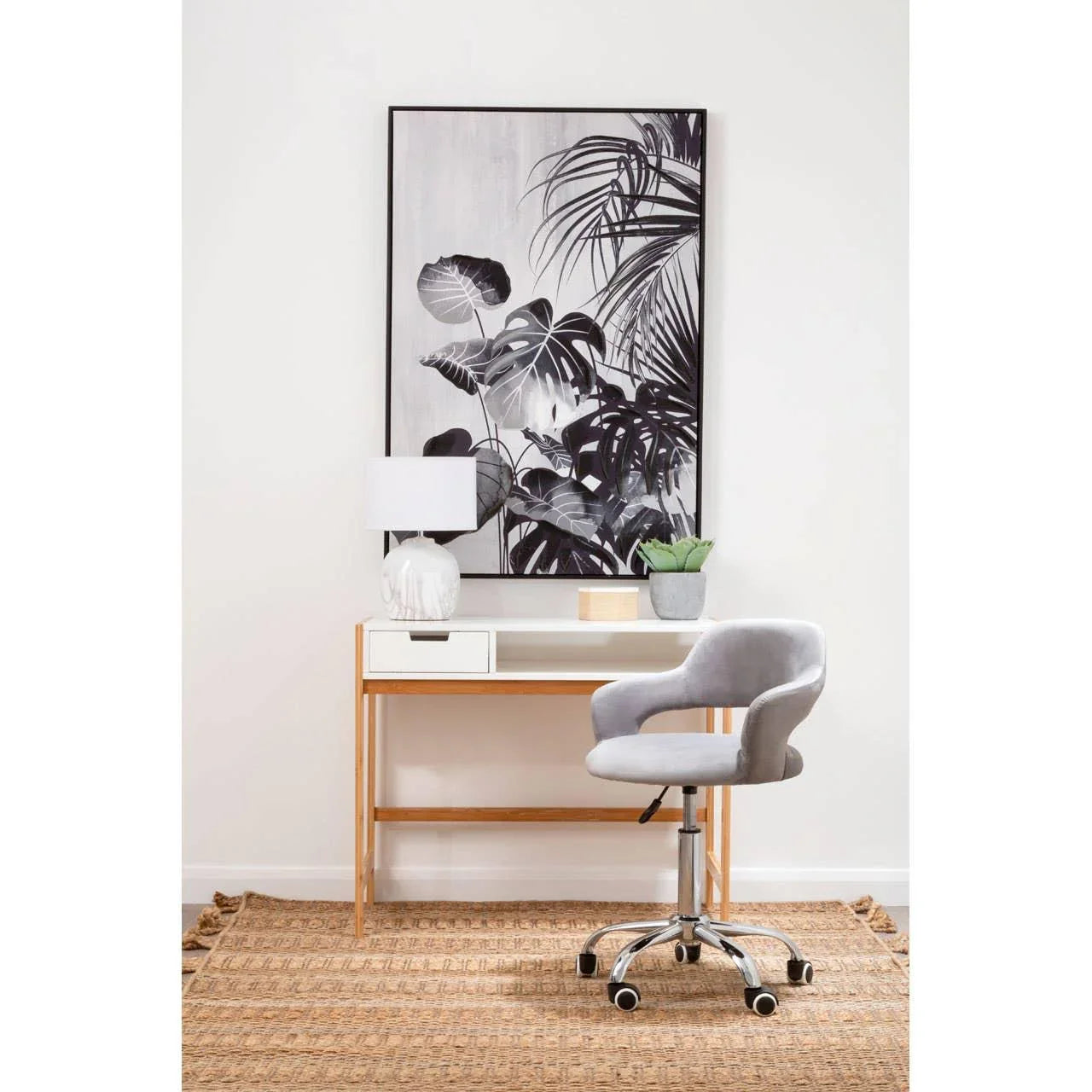 Grey office chair with chrome base by wooden desk, lamp, and plant in modern home workspace
