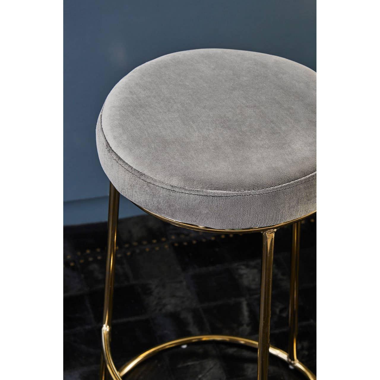 Grey velvet bar stool with round gold legs on dark floor