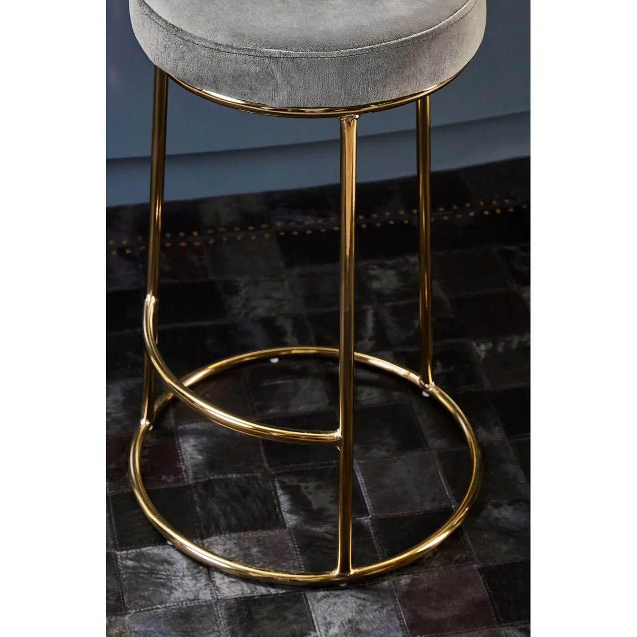 Grey velvet bar stool with gold metal frame on dark tiled floor