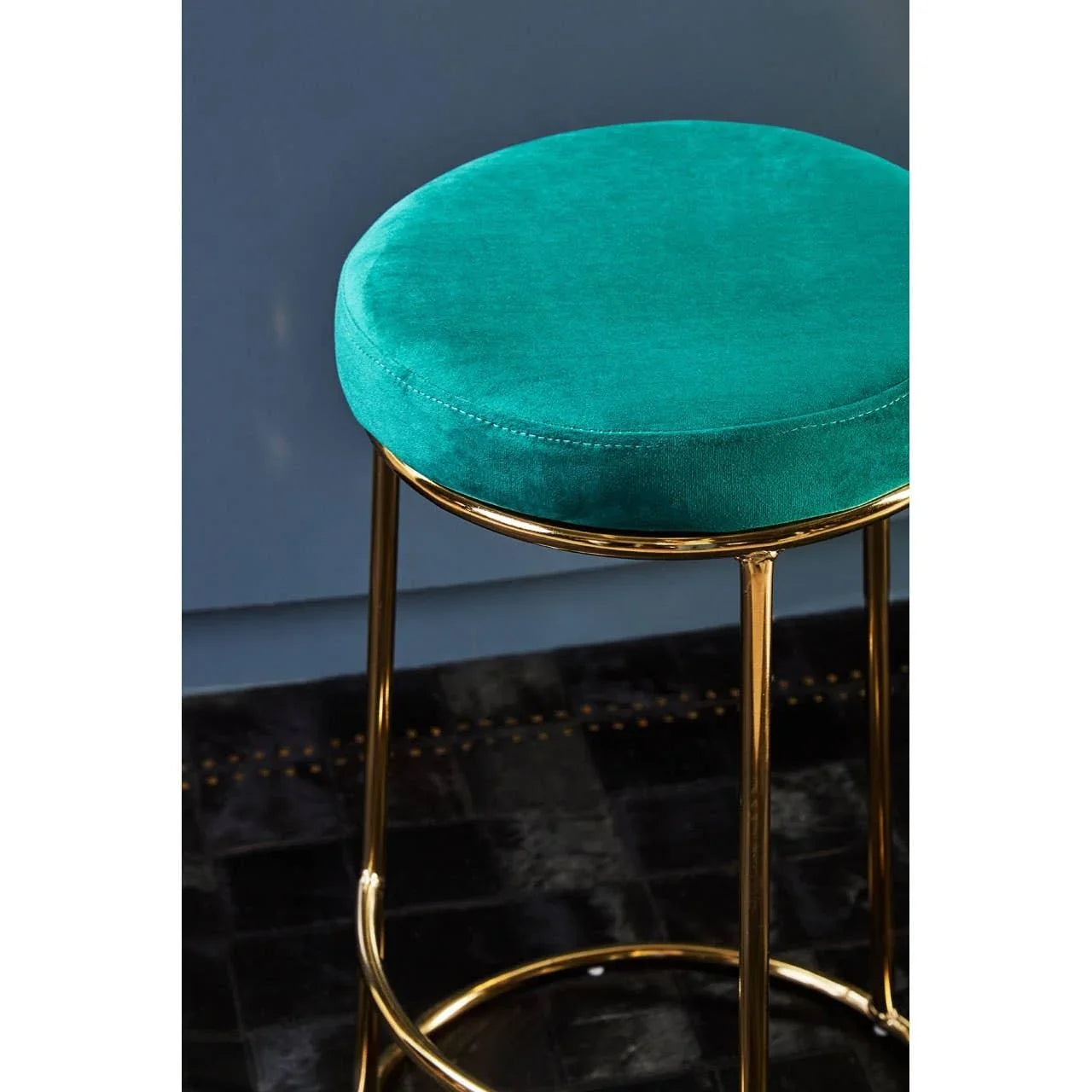 Velvet bar stool with teal seat and gold metal legs on black rug