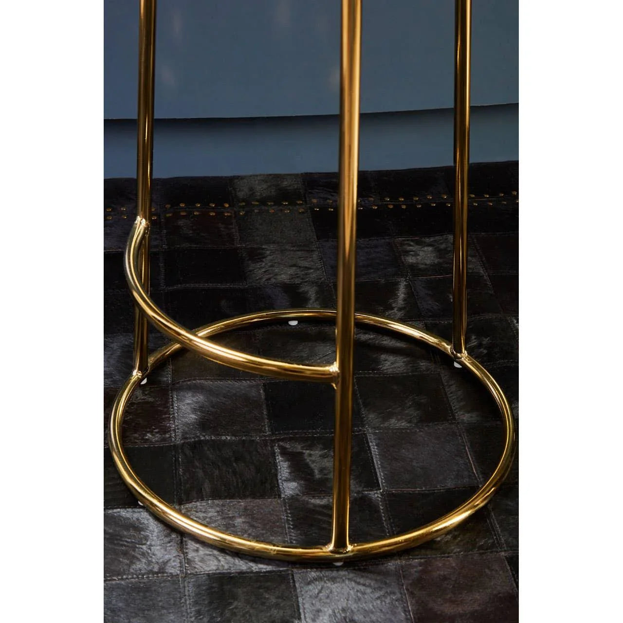 Gold metal bar stool legs with circular footrest on dark leather patchwork rug