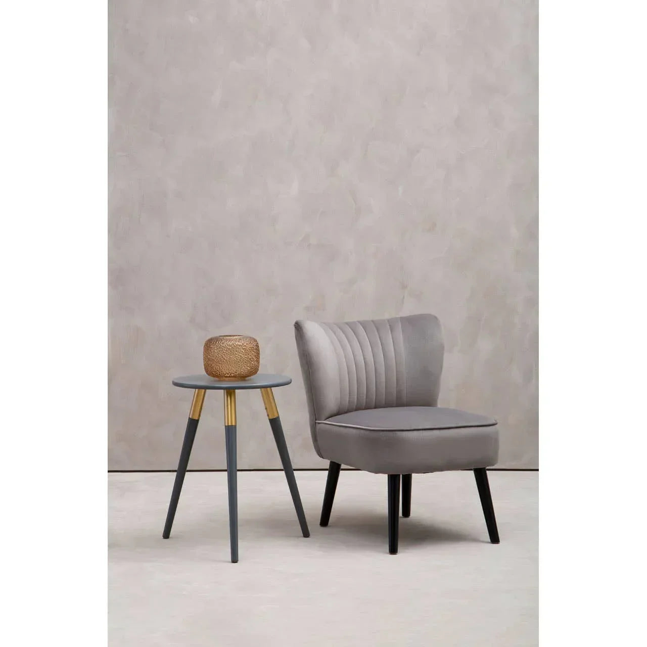 Grey velvet accent chair with fluted backrest beside round side table with gold accents