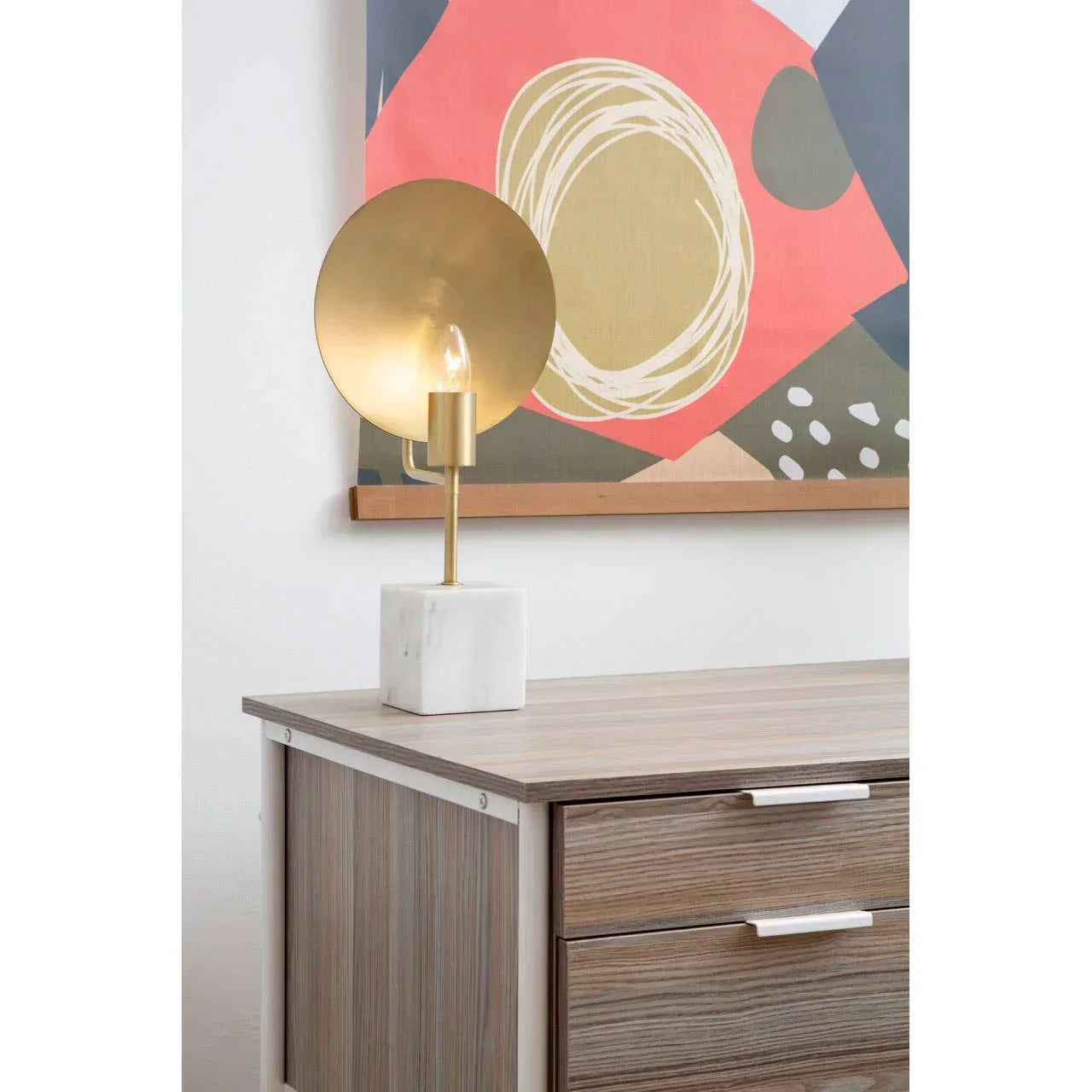 Modern table lamp with gold disc shade and marble base on wood cabinet