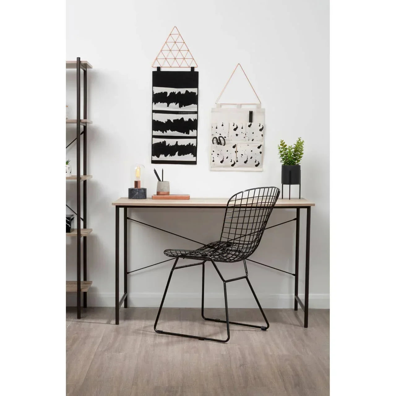 Modern home office desk with metal frame and wire chair against white wall decor