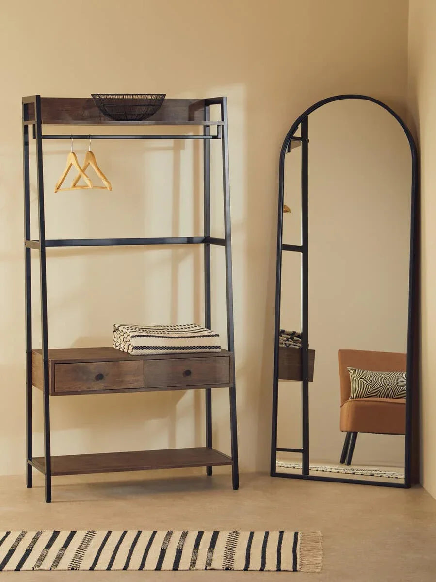 Industrial clothes rail with wooden shelves and drawers beside arched full length mirror