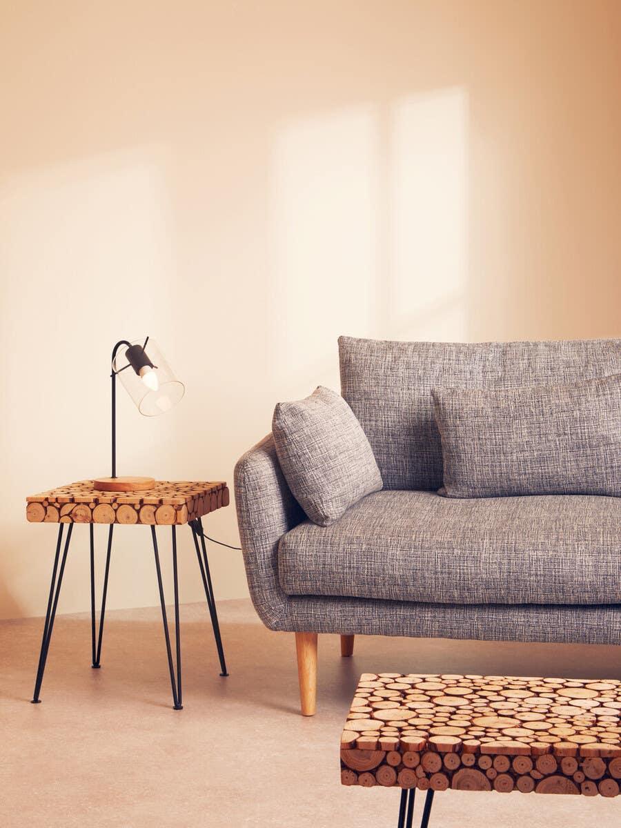 Grey fabric sofa with wooden legs beside a round wood slice side table and black lamp