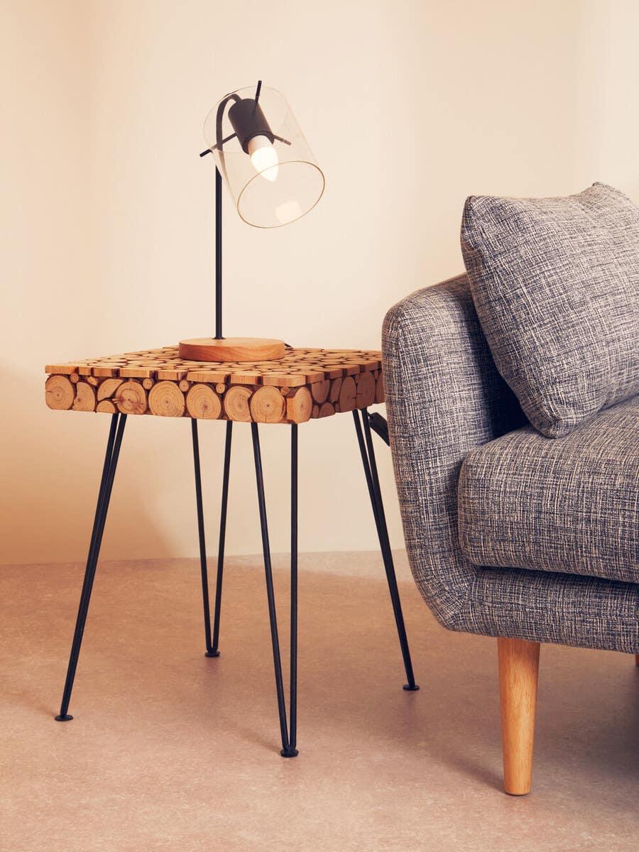 Wood slice top side table with black metal legs beside a grey sofa and modern table lamp