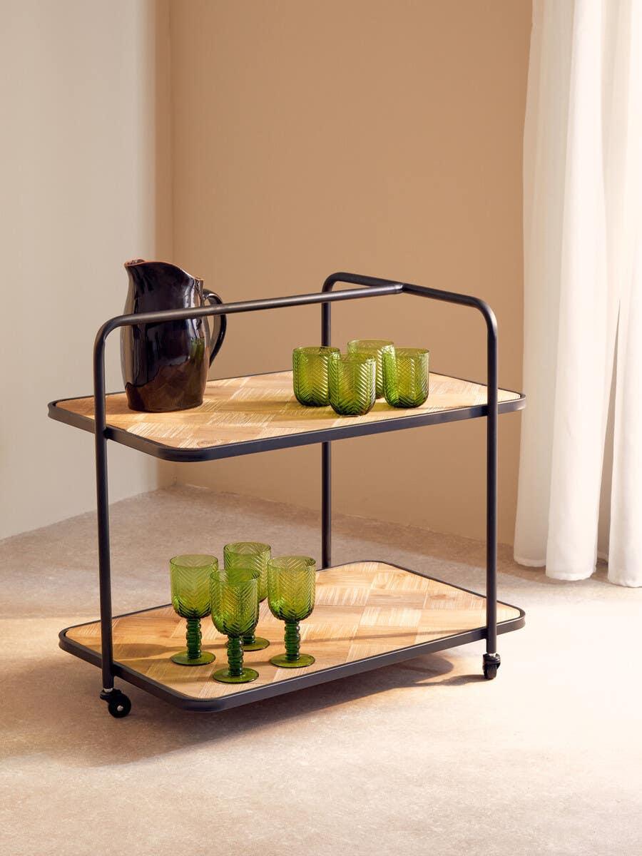 Two-tier wooden drinks trolley with black metal frame, green glasses and dark jug