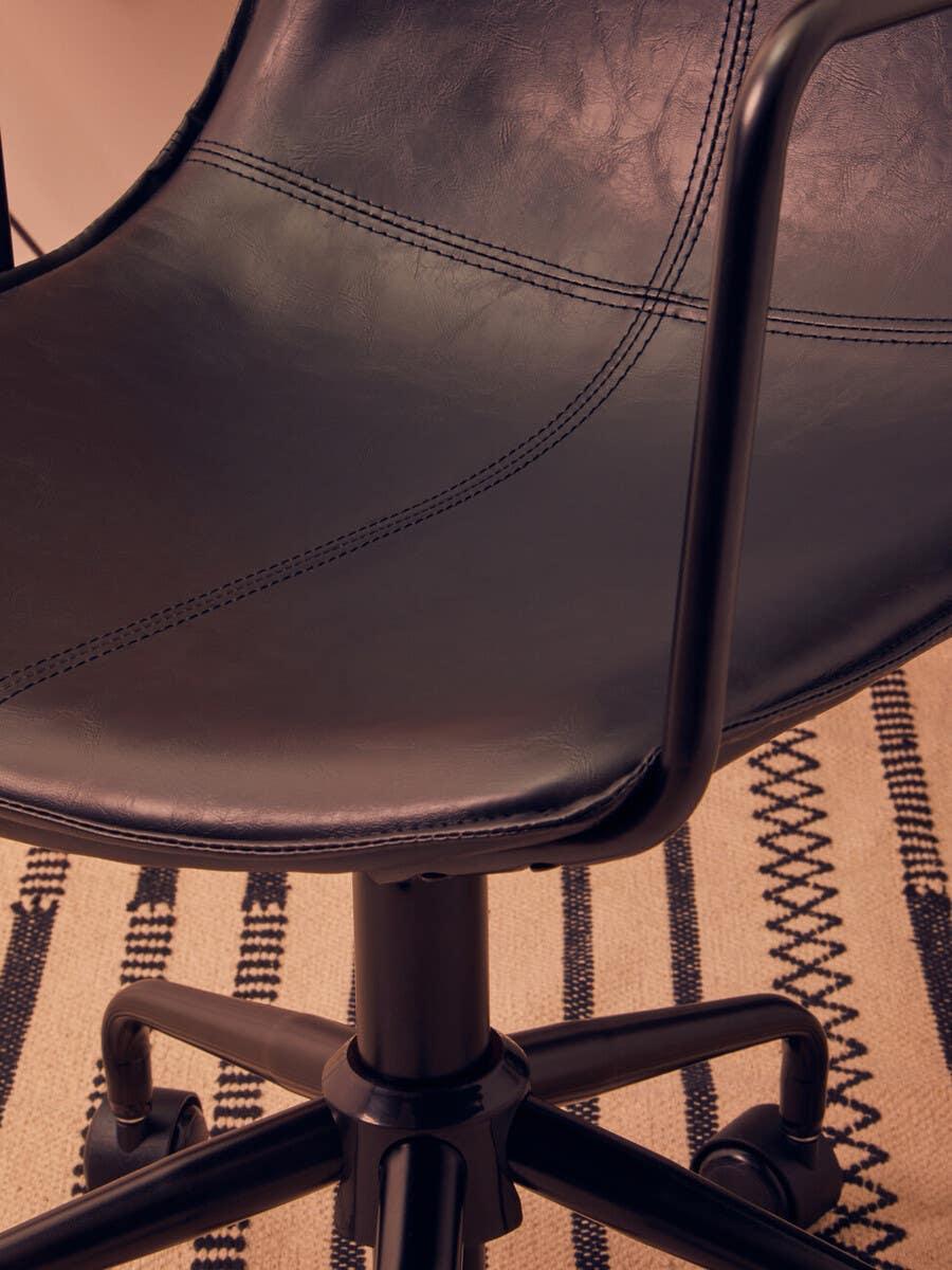 Black leather office chair seat with stitching detail and metal legs on patterned rug