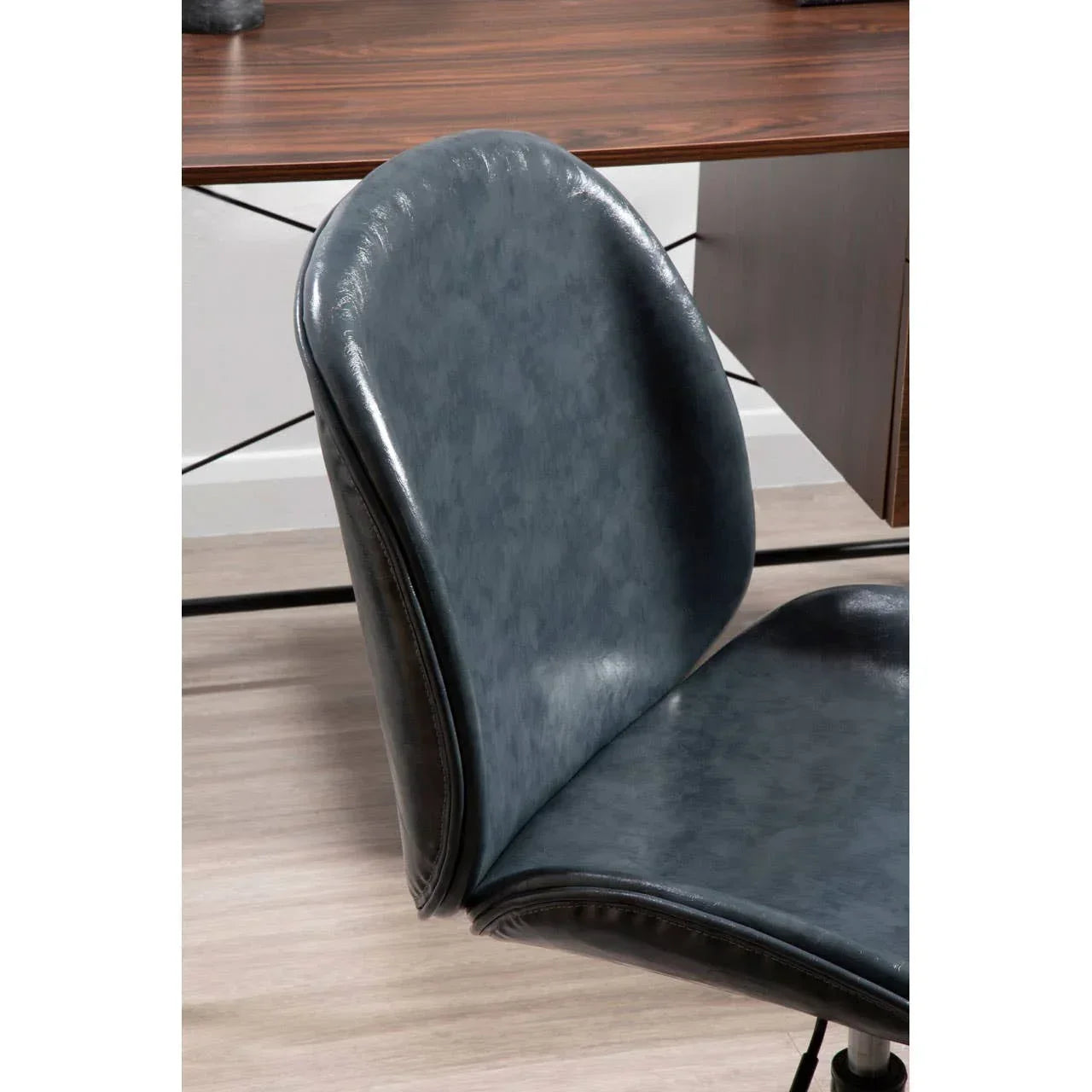 Blue faux leather office chair with curved backrest next to wooden desk on light flooring