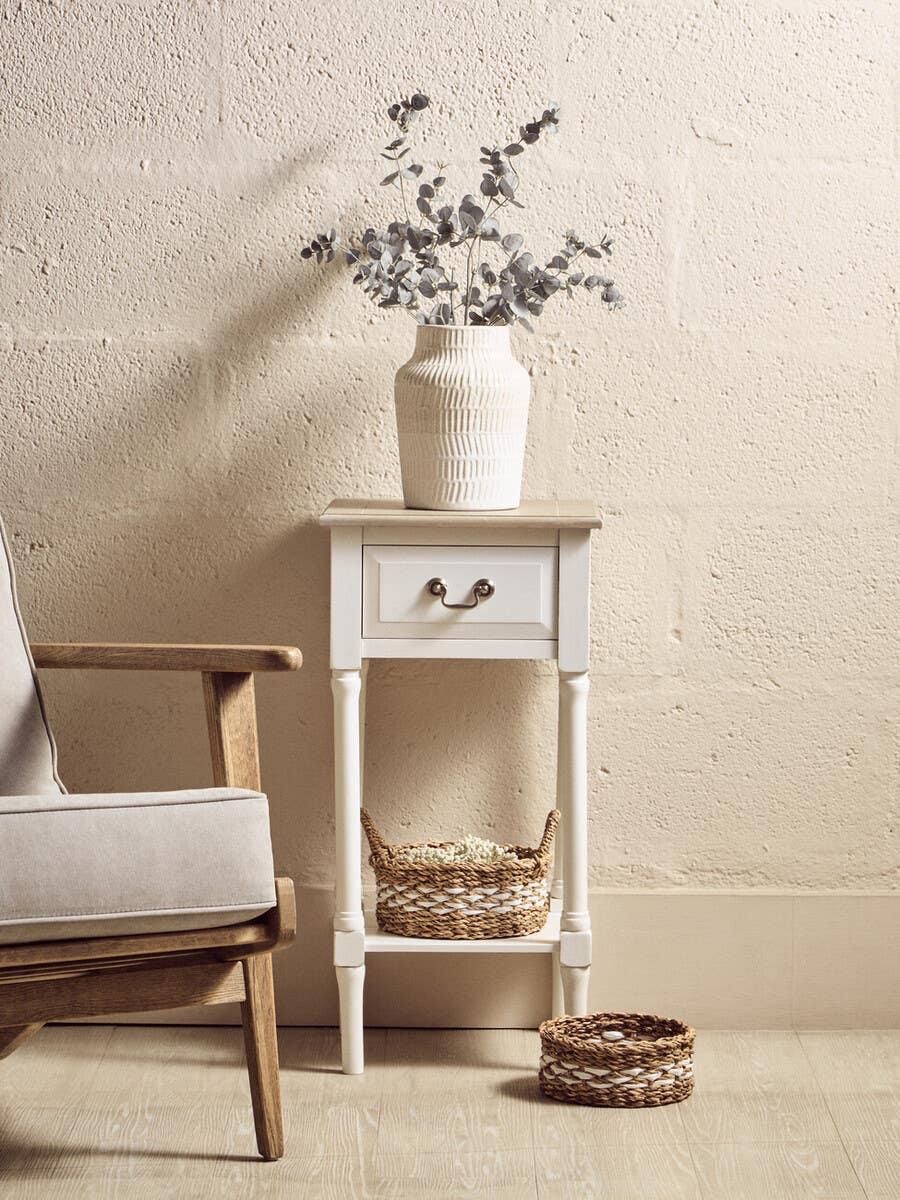White wooden side table with drawer and wicker baskets, vase with eucalyptus branches on top