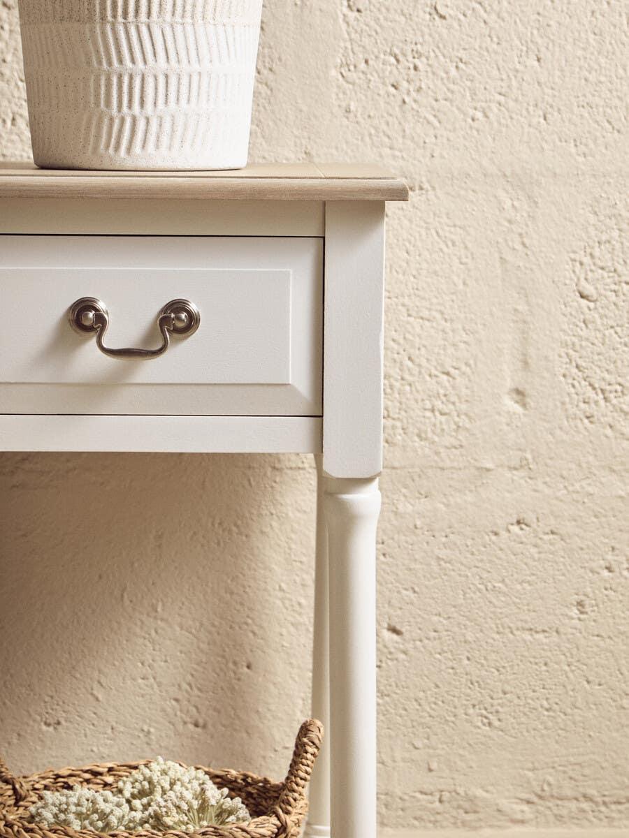 White wooden bedside table with metal handle, wicker basket and textured ceramic planter