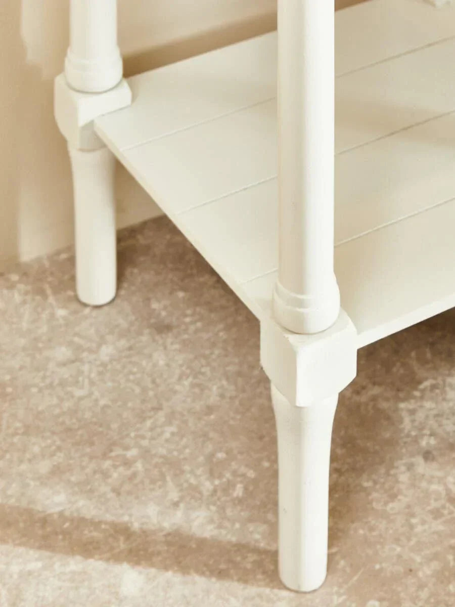 Close view of white wooden table legs and lower shelf on stone floor