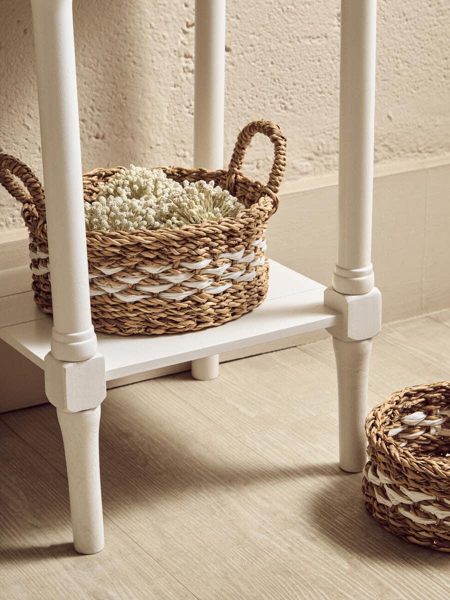 Woven seagrass storage basket with handles and white accent under a cream wooden side table