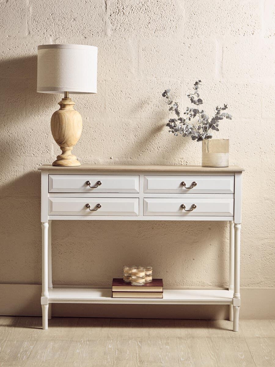 White hallway console table with four drawers, wood lamp, vase and books on lower shelf