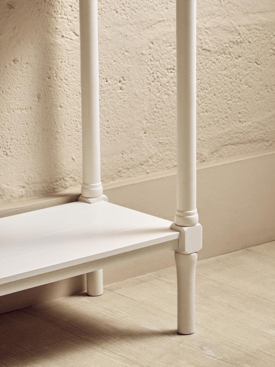 Close-up of cream painted wooden furniture leg and lower shelf on light wood flooring