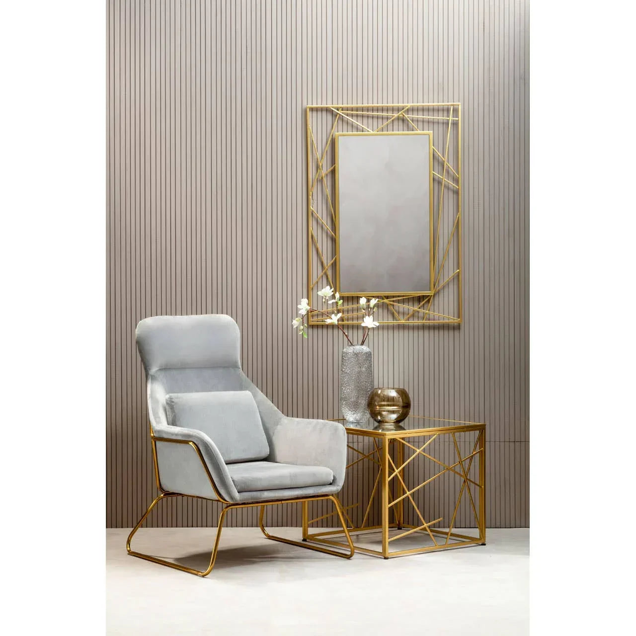 Grey velvet accent chair beside gold metal side table and geometric framed wall mirror