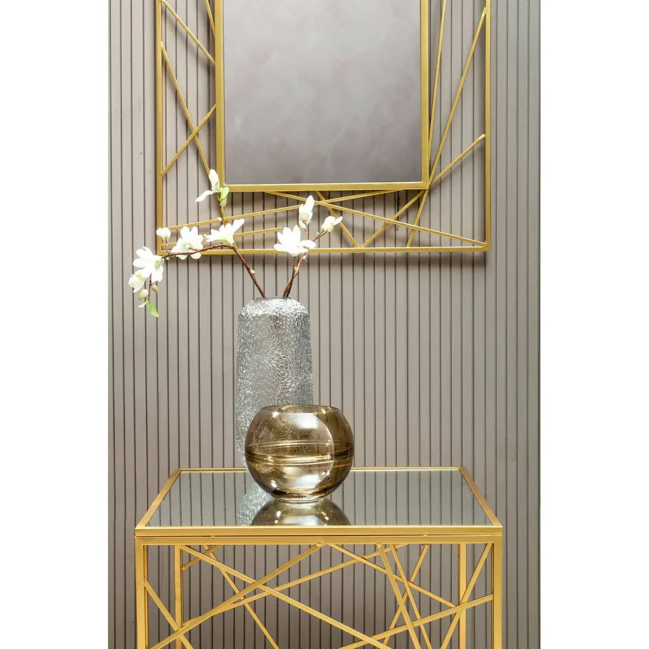 Gold geometric console table with glass top, decorative vases, and matching wall mirror