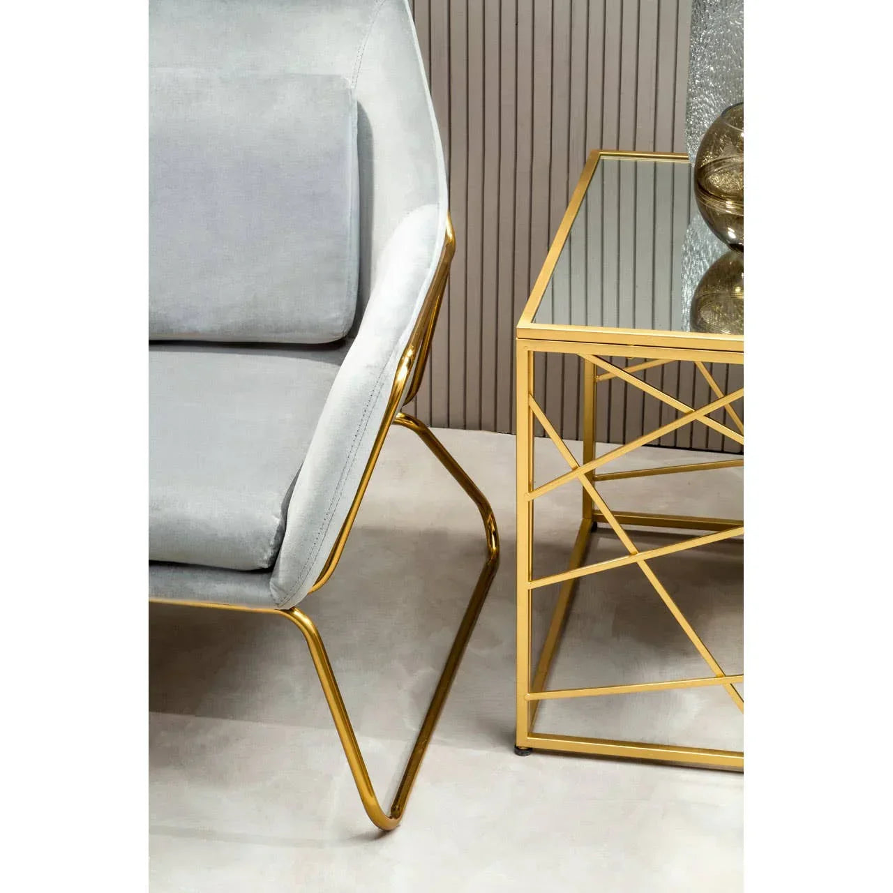 Grey velvet chair with gold metal frame beside mirrored gold side table