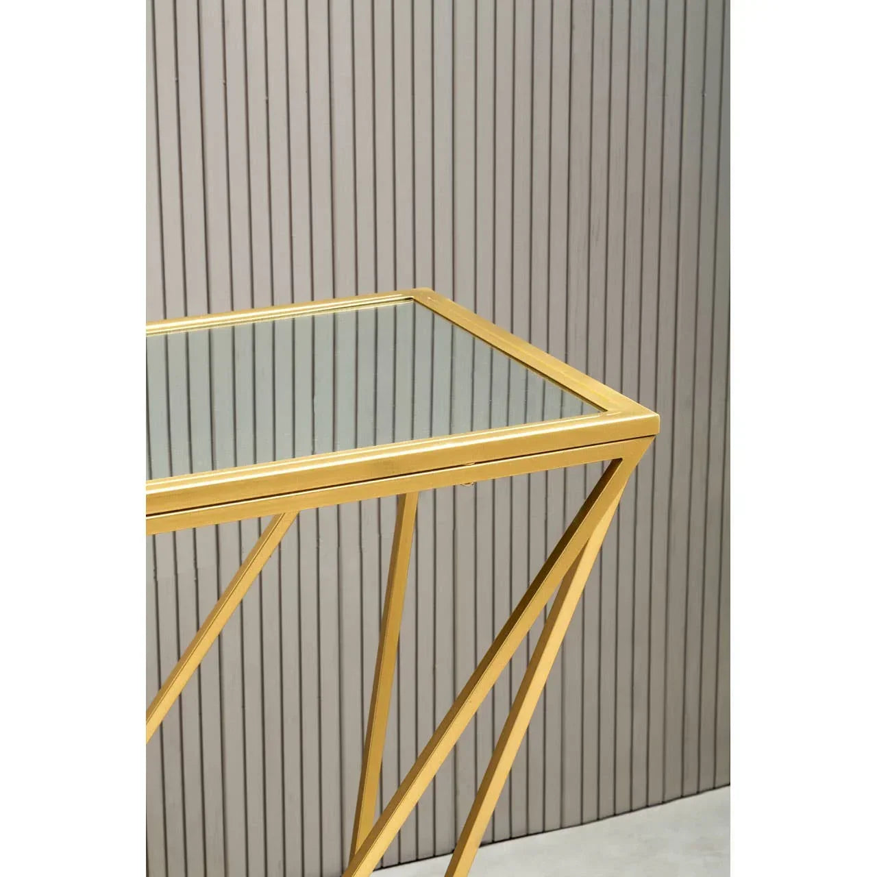 Gold metal and glass side table with geometric legs against a slatted wall