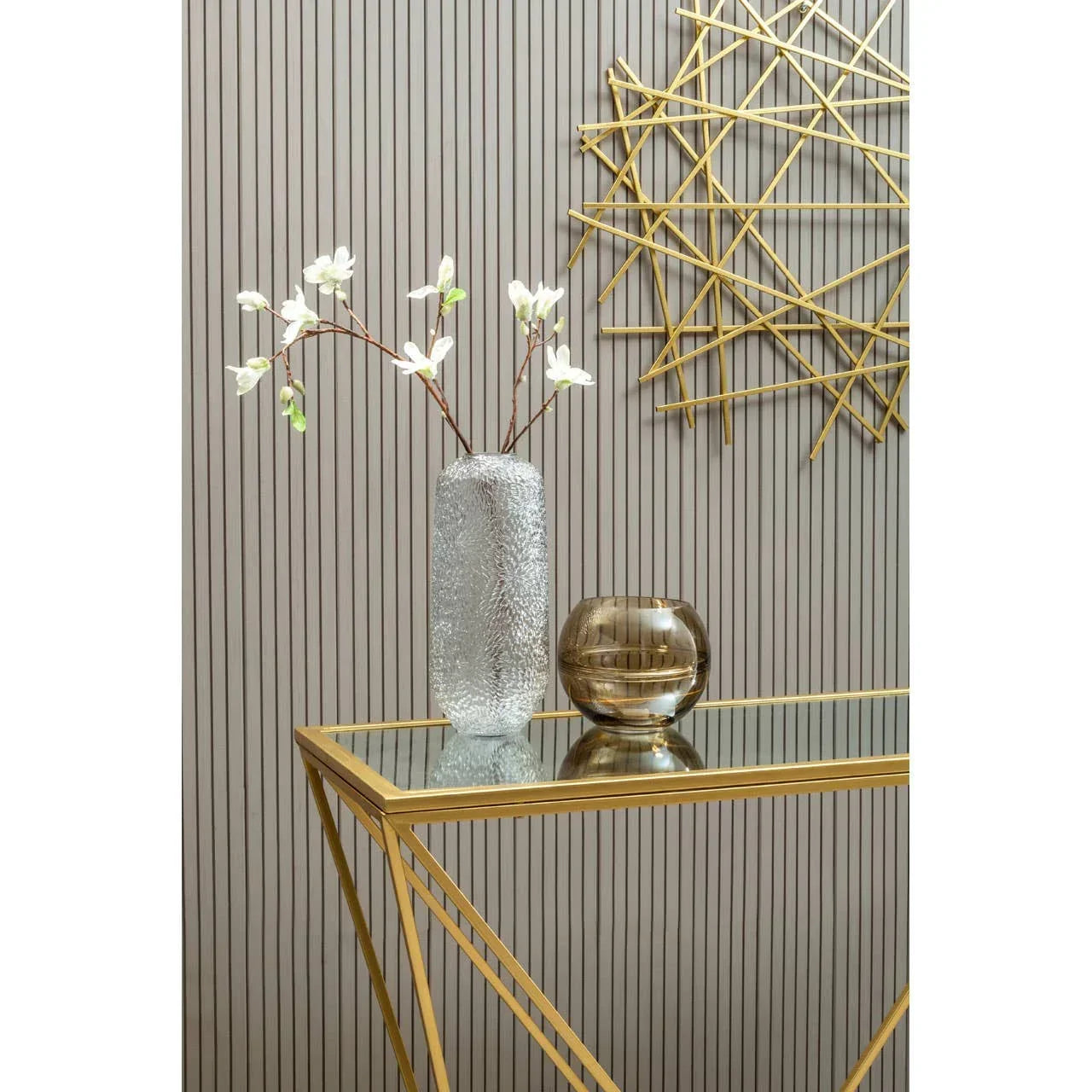 Gold metal console table with glass top, decorative vases, wall art and panel background