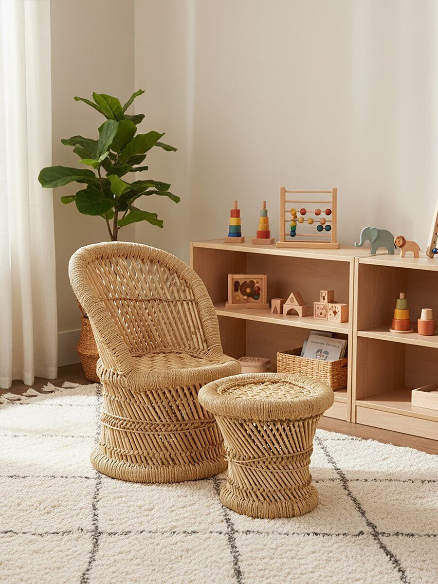 Natural woven bamboo chair and stool set designed for children, featuring a curved chair with a comfortable backrest and a matching round stool. The furniture is placed in a bright, airy room with a light-colored rug and wooden shelving displaying colorful toys and decor. A green plant adds a touch of nature to the space
