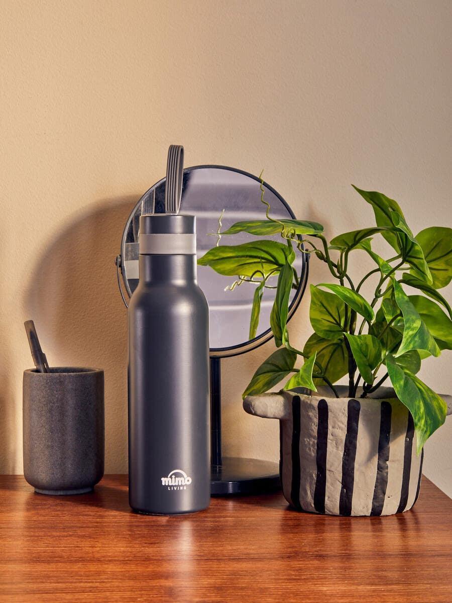 Matte black water bottle on wooden table beside ceramic plant pot and mirror
