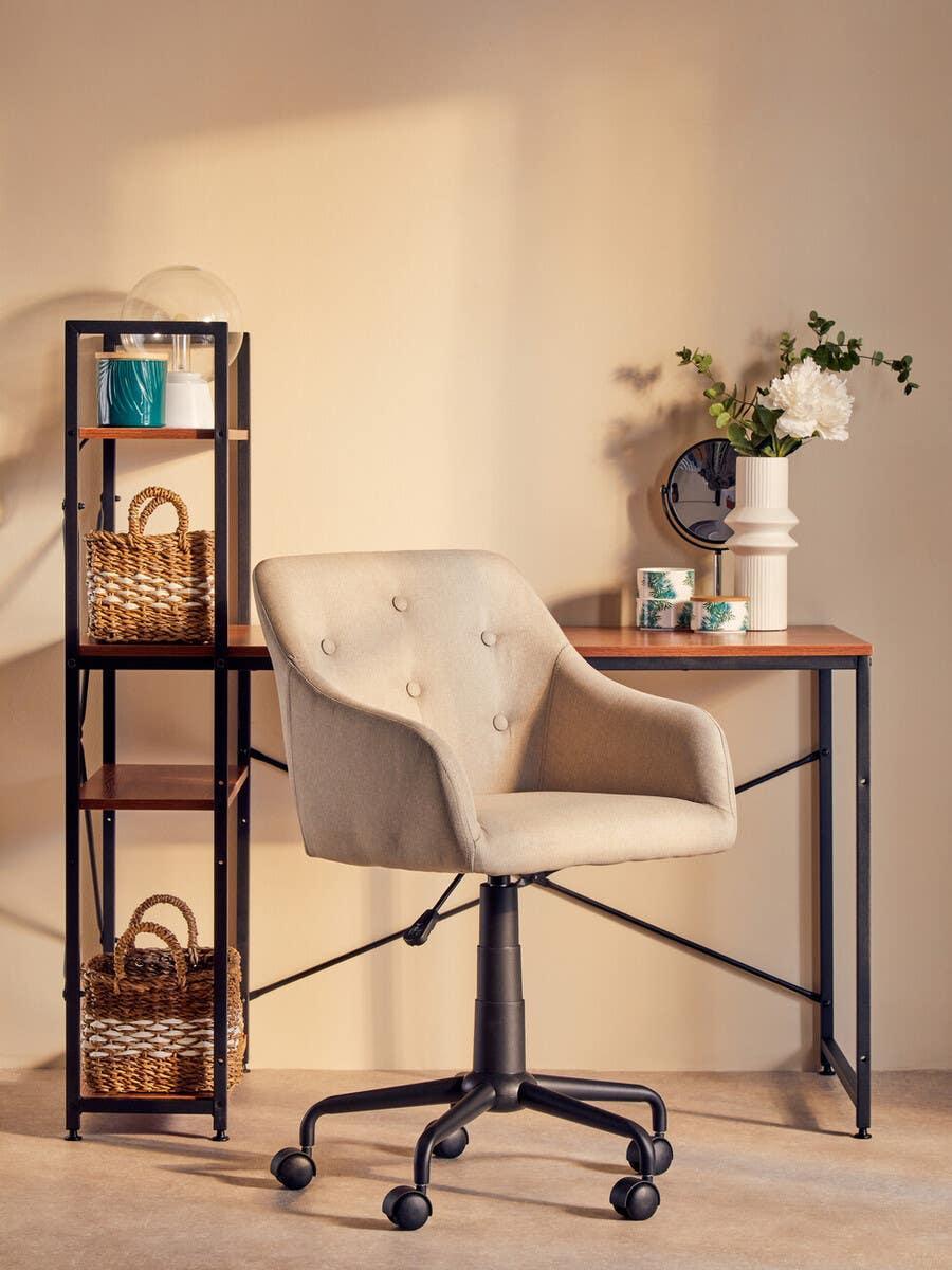 Beige fabric office chair on wheels beside wooden desk with metal frame and storage shelf