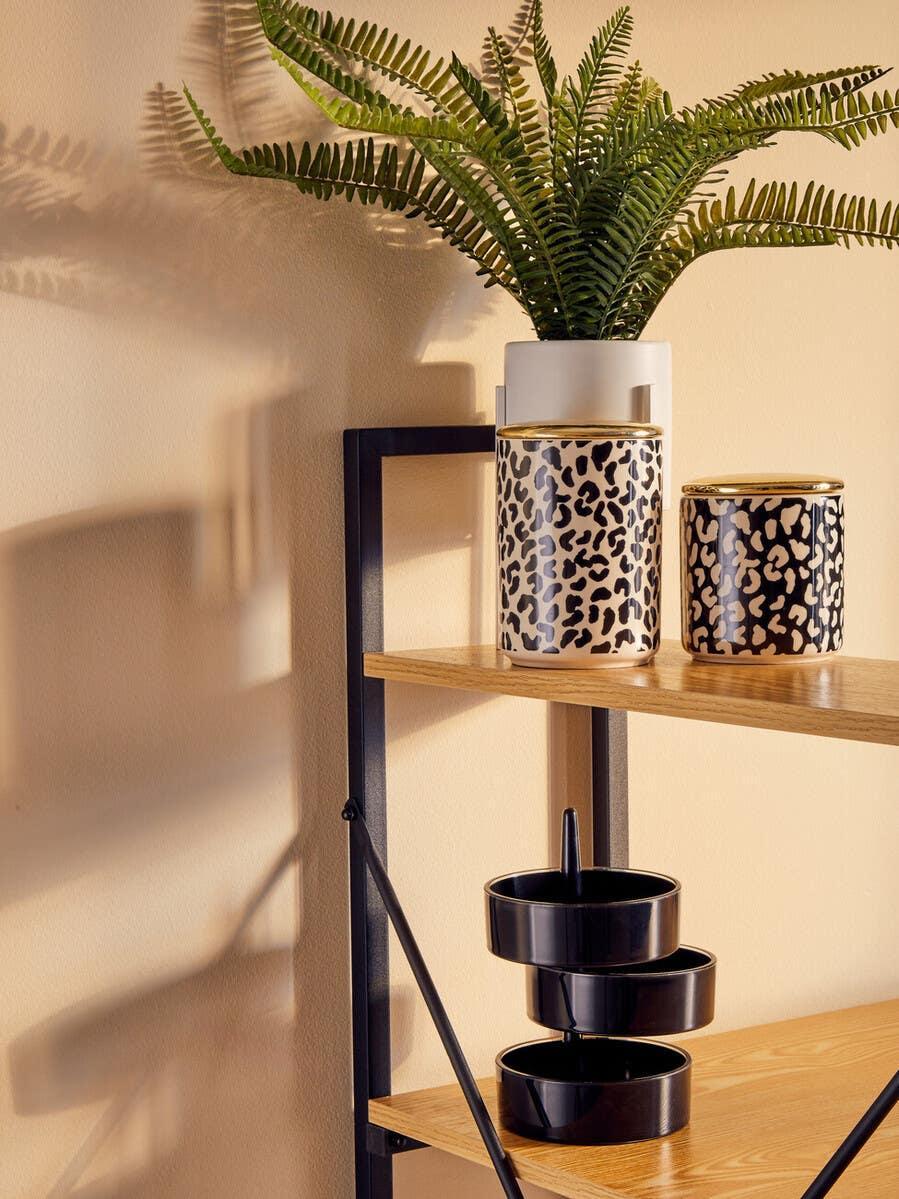Leopard print storage jars and potted fern on wooden shelving unit with black metal frame
