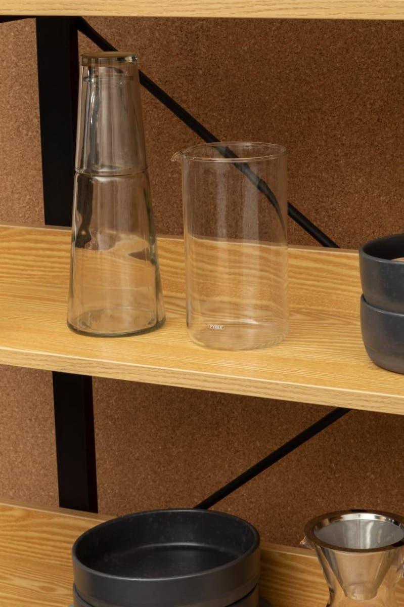 Wooden shelving unit with glass carafe, glass jug, stacked black bowls and metal funnel