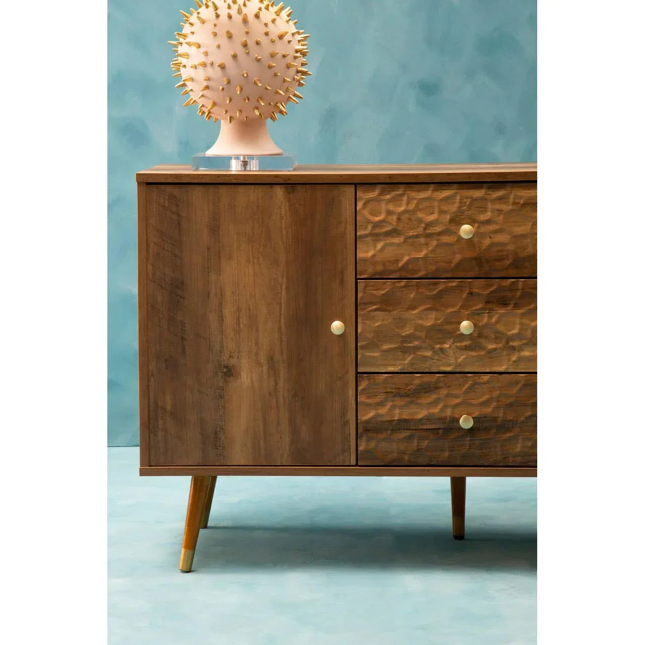 Walnut sideboard with textured drawers and gold knobs on blue background